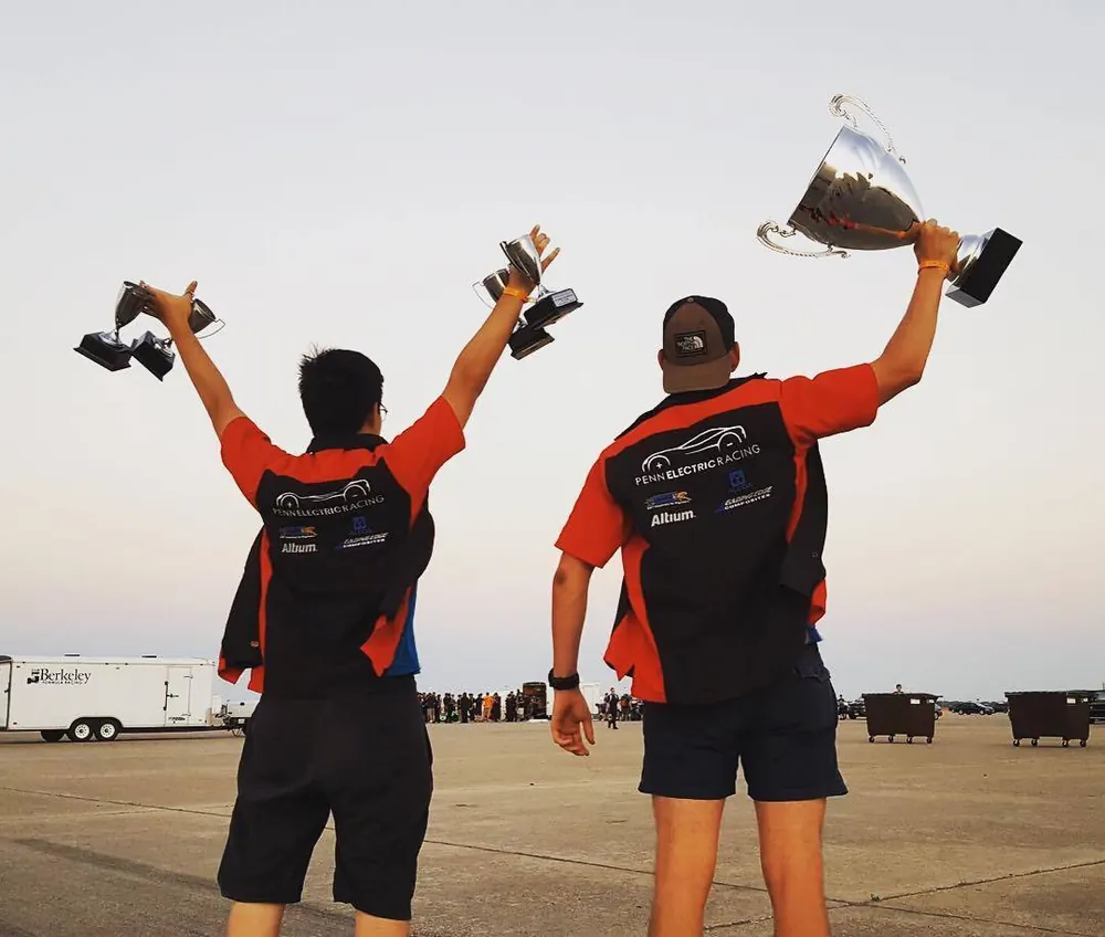 Two team members hold trophies above their heads at competition