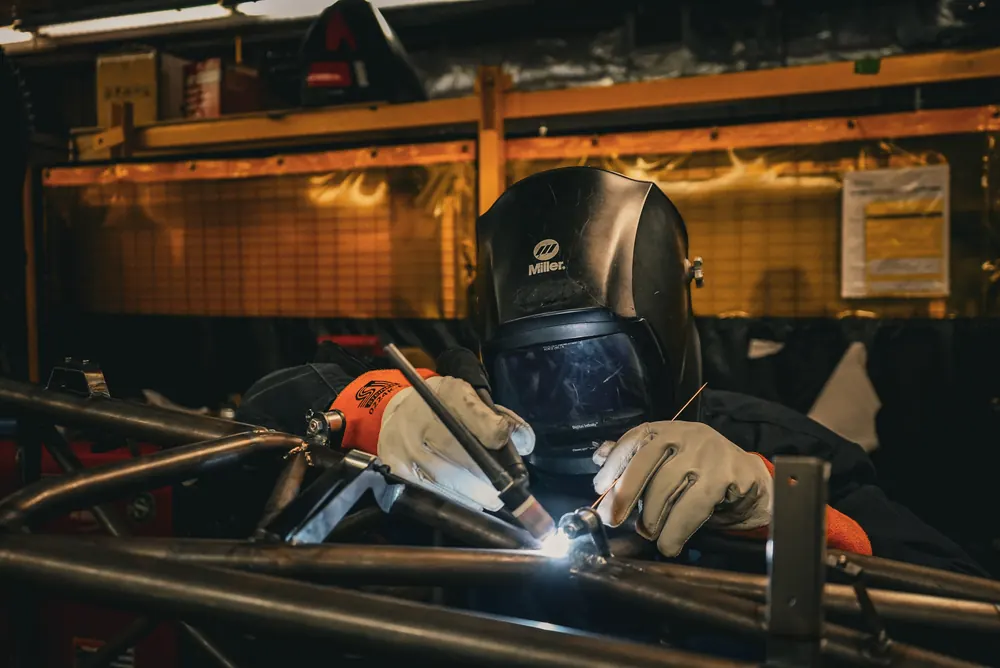A team member in a welding helmet welds the steel frame